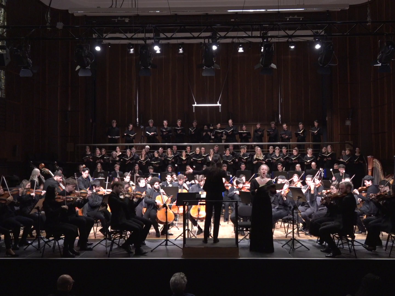 Frontalansicht auf Bühne mit Chor, Orchester, Sopranistin und Dirigentin
