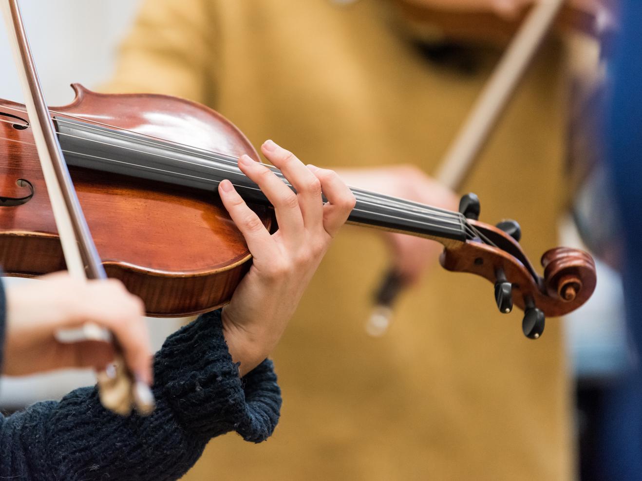 Nahaufnahme einer Bratsche bzw. Viola, die von zwei Händen in einem blauen Strickpulli gespielt wird.