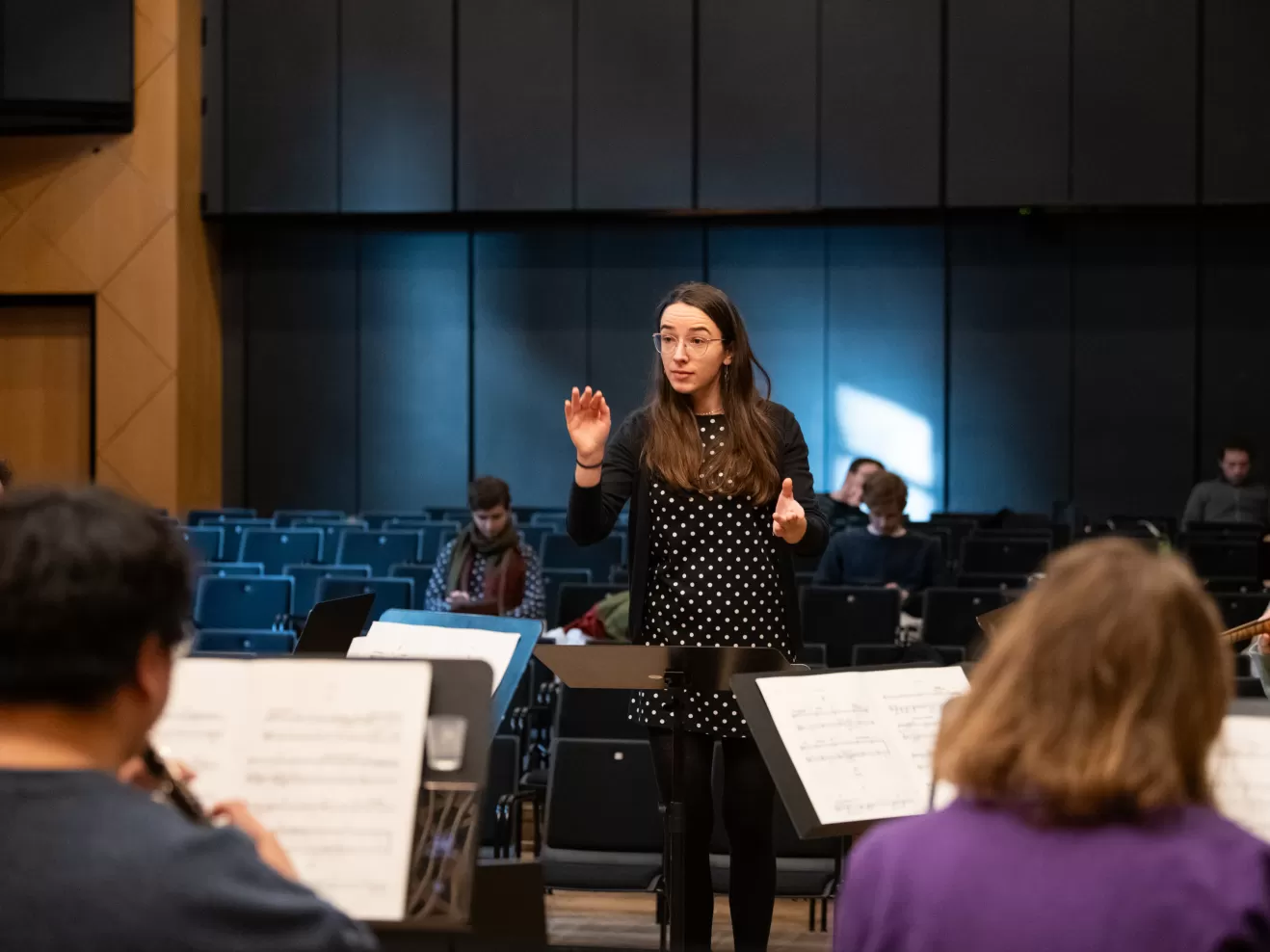 Dirigentin vor einem kleinen Ensemble, fotografiert aus der Perspektive der Musiker*innen