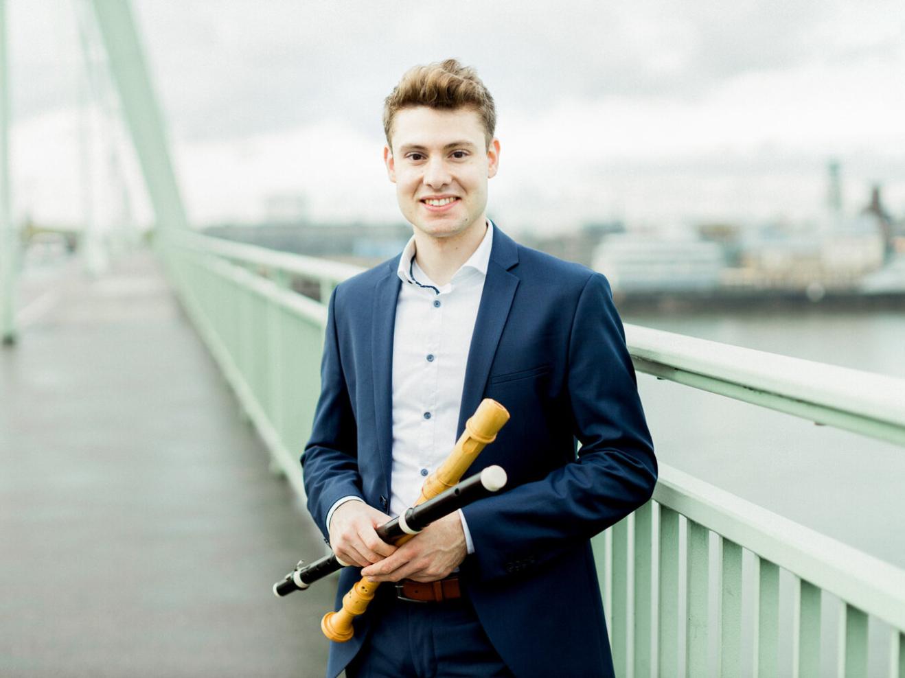 Sebastian Schmidt steht auf einer Brücke, in der Hand hält er eine Blockflöte und eine Traversflöte.