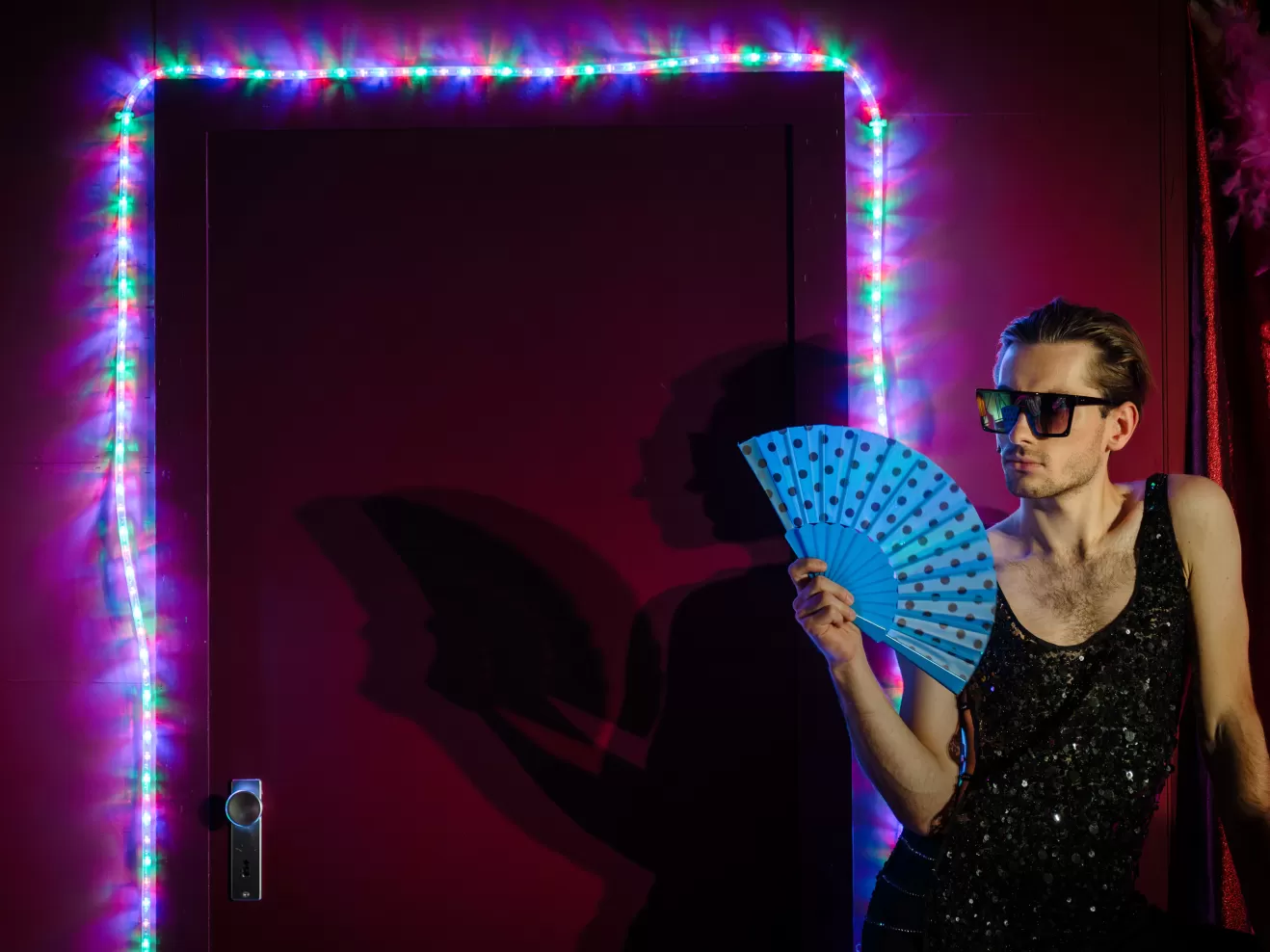 Ein Mann mit Sonnenbrille und Fächer vor einer bunten Lichterkette.