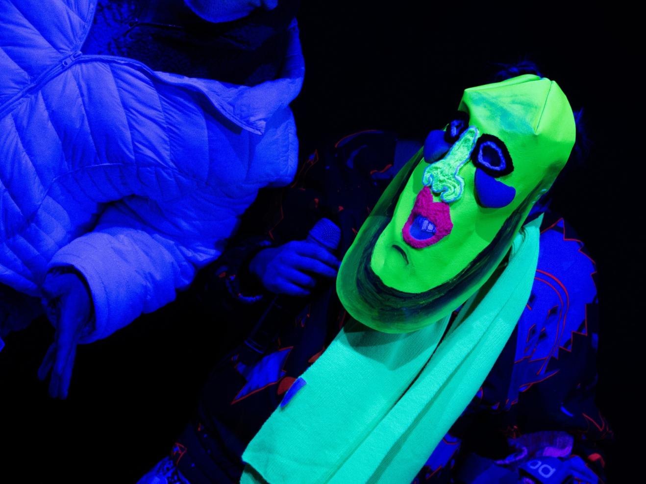 Zwei Figuren mit Masken im Schwarzlicht.