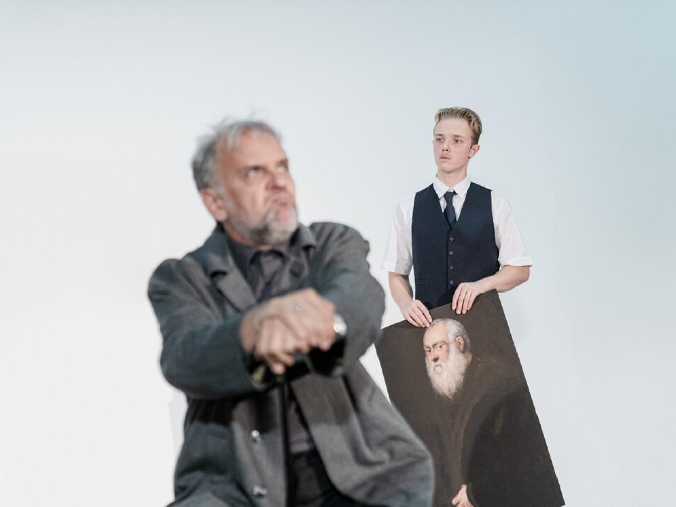 Ein Mann mit Bild in der Hand guckt einen anderen Mann schräg an