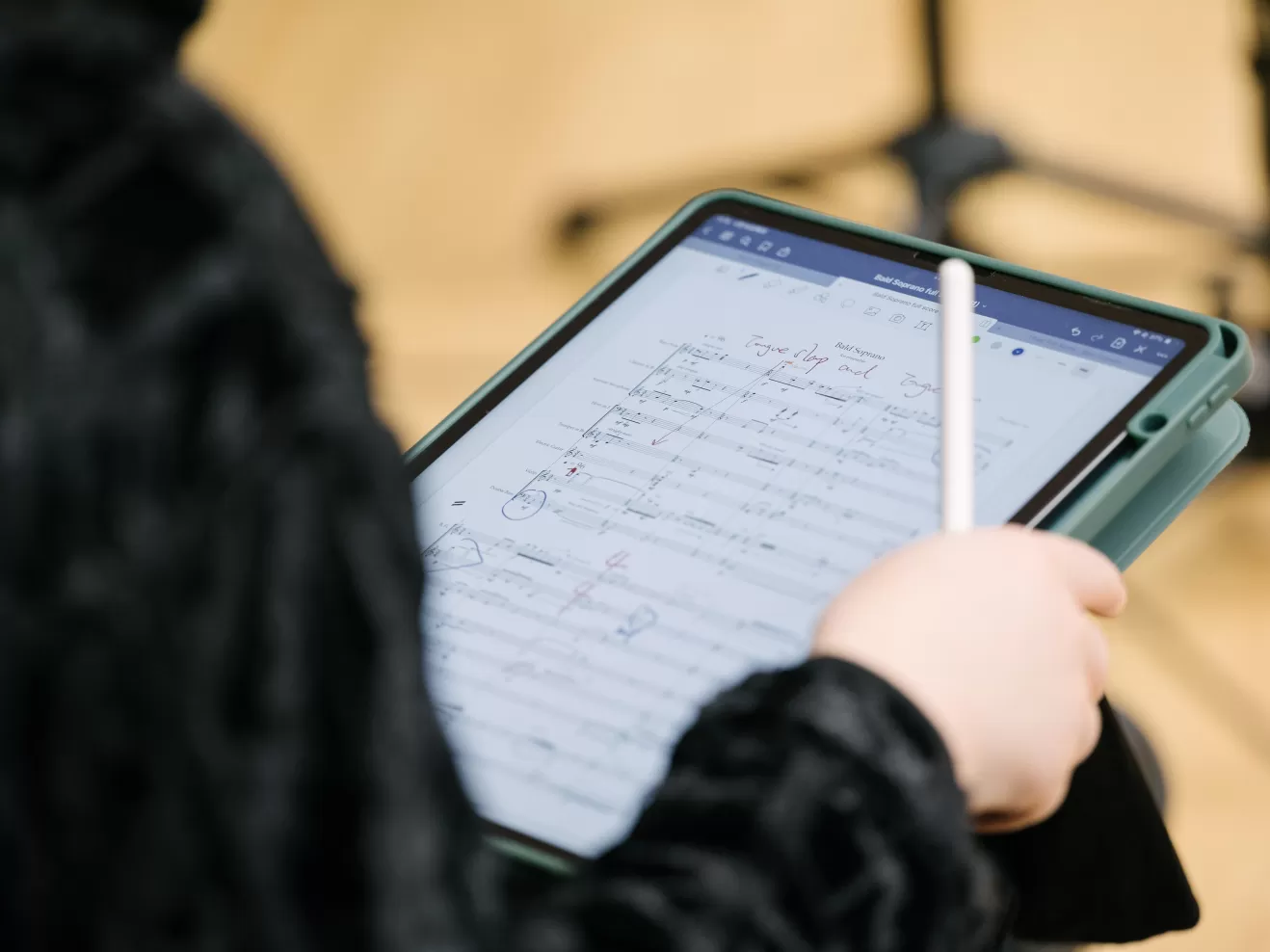 Nahaufnahme eines Tablet-Computers auf den Knien einer Person, die einen Stift in der Hand hält. Auf dem Display sind Noten zu sehen.