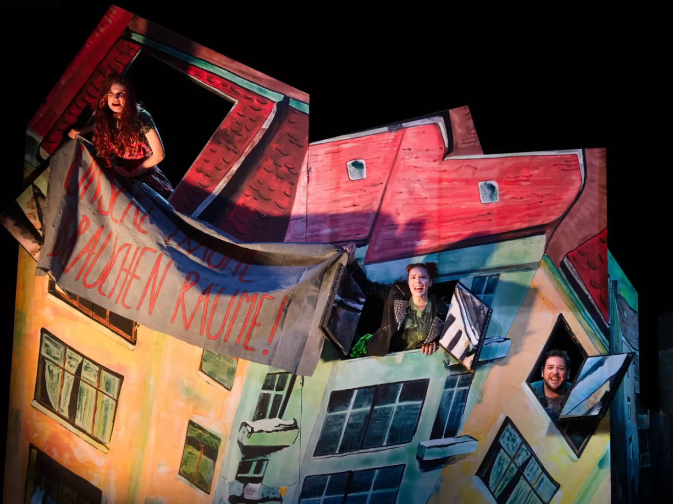 Zwei Menschen schauen aus einem Haus und halten einen Banner.