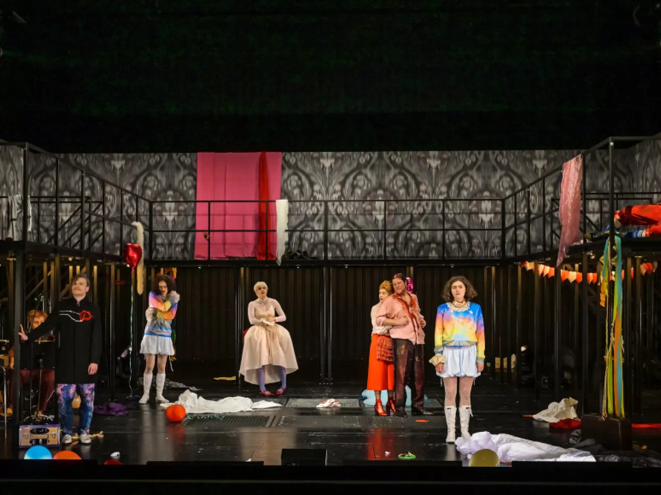 Eine Personengruppe in bunter Kleidung steht versetzt auf der Bühne