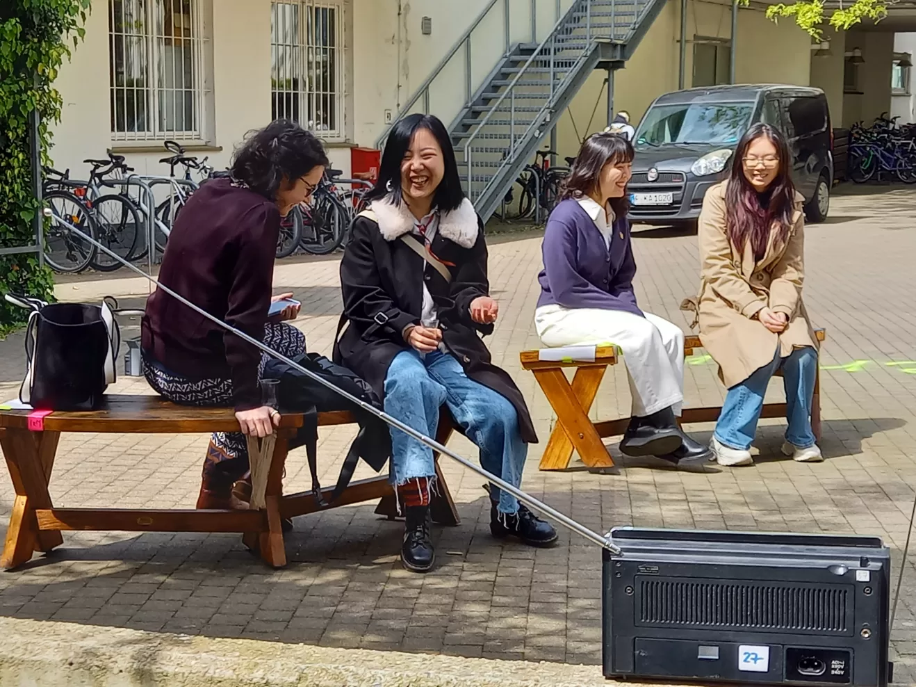 Studierende sitzen lachend im Innenhof. Im Vordergrund steht ein Radiogerät.