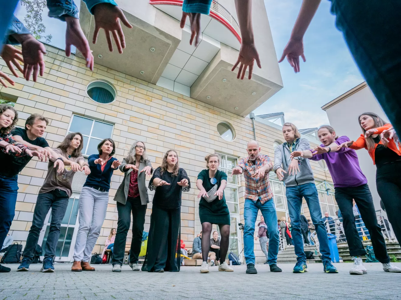 Eine Gruppe Menschen steht in einem Kreis und streckt die Hände in die Mitte.