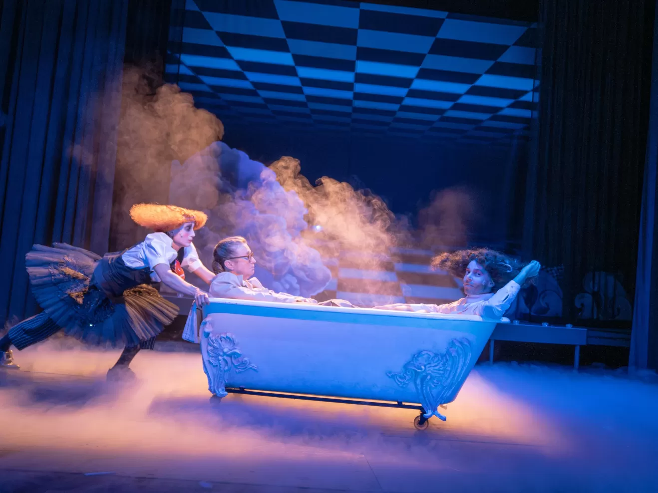 Lisa Freiberger schiebt eine Badewanne über die Bühne, in der zwei Menschen sitzen.