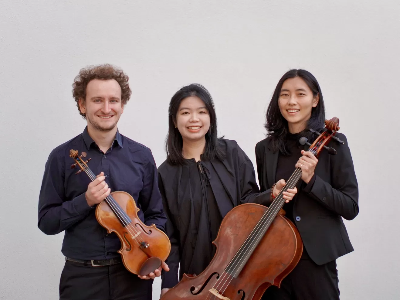 Die drei Musiker*innen des Pollux Trios, lachend mit Instrumenten