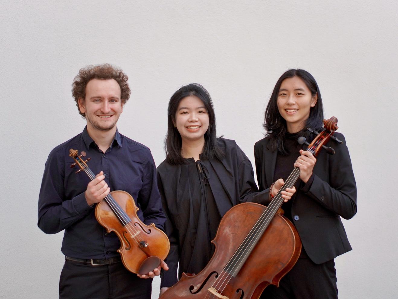Die drei Musiker*innen des Pollux Trios, lachend mit Instrumenten