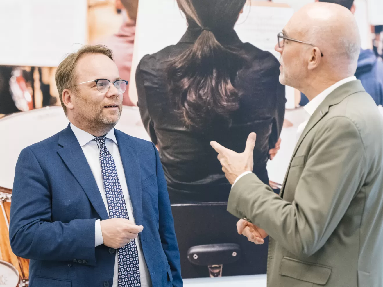 Timon Gremmels und Prof. Elmar Fulda, beide tragen Anzug, unterhalten sich vor dem großen Bild einer Musikerin
