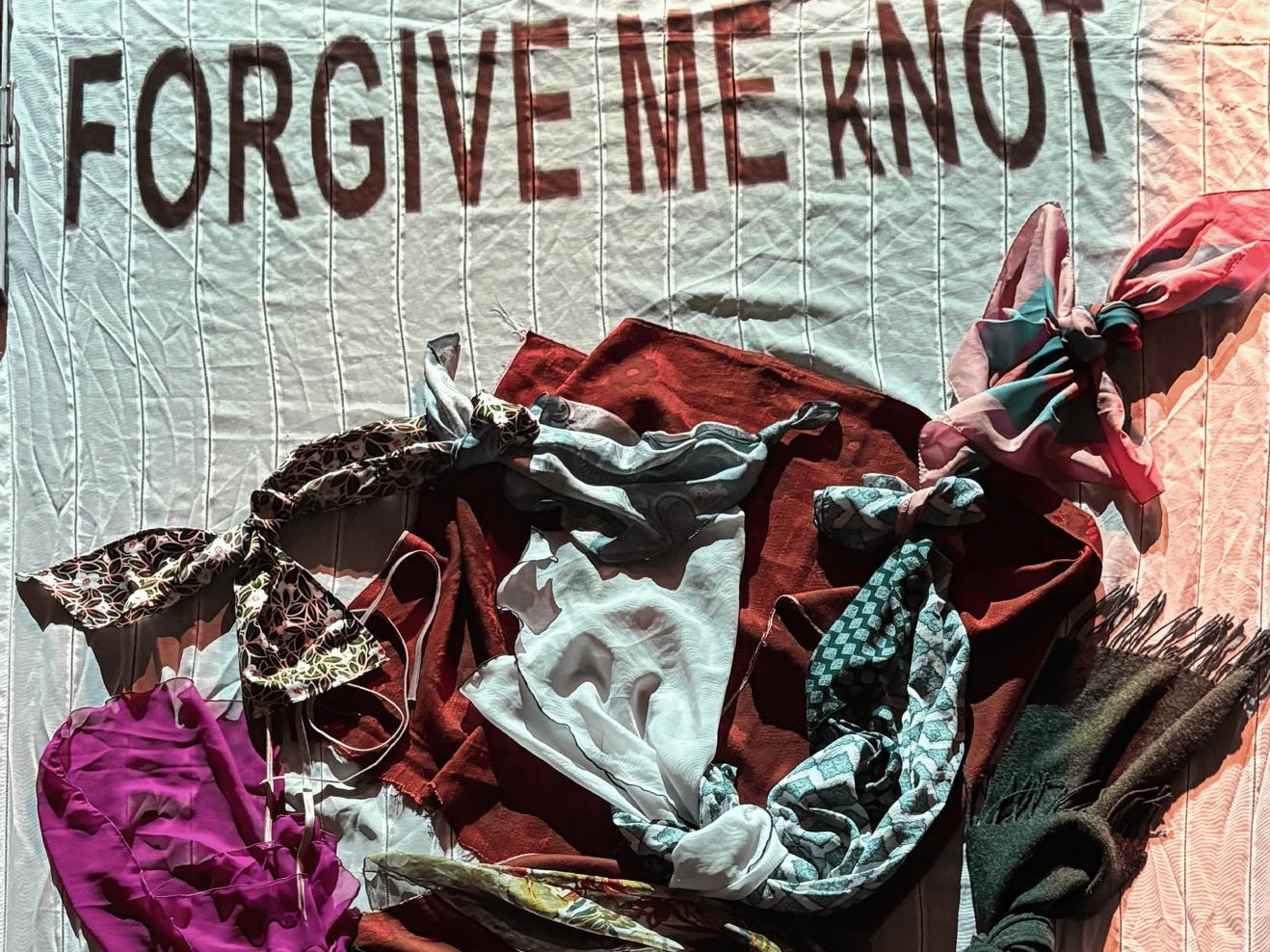 Das Plakat zur Aufführung zeigt einen Haufen bunter Stoffe, die ineinander liegen und teils verknotet sind. Am oberen Bildrand steht der Titel "FORGET ME (K)NOT".