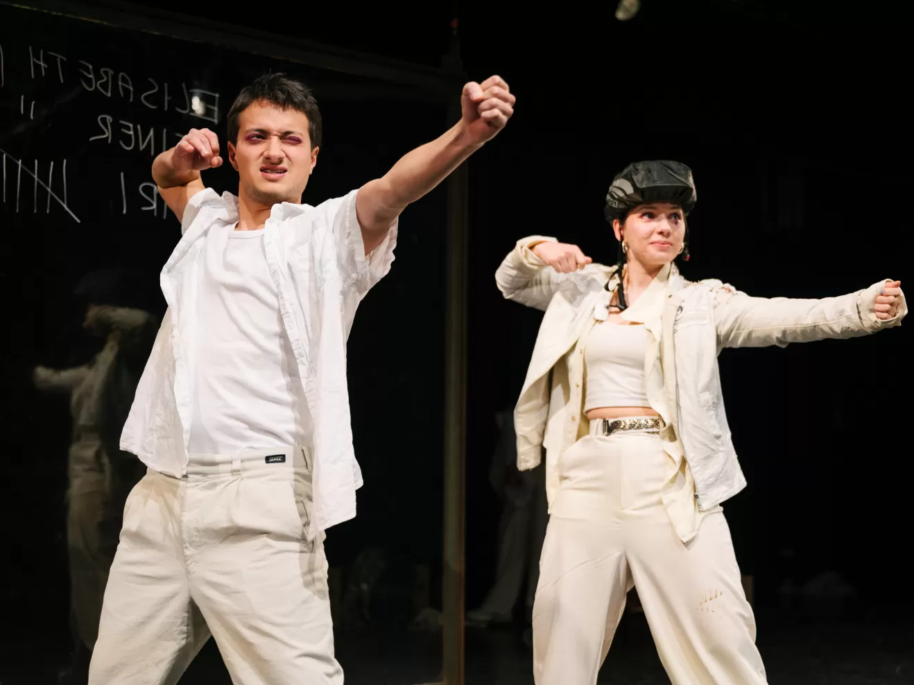 Zwei ganz in weiß gekleidete Schauspieler*innen machen eine Bogenschieß-Bewegung