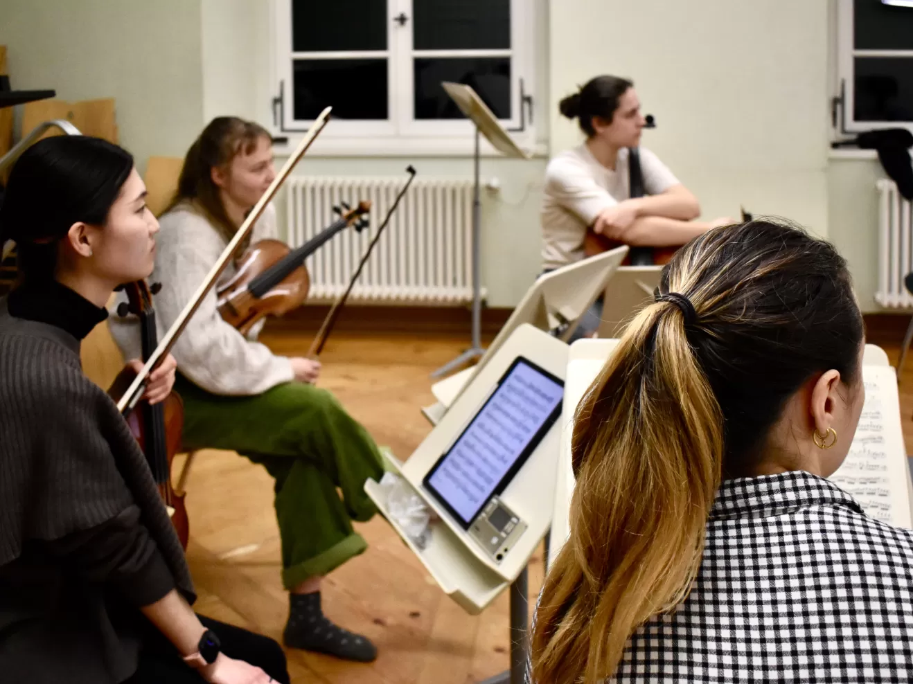 Vier Musikerinnen sitzen mit Instrumenten in einem Proberaum vor einem Fenster und blicken nach rechts