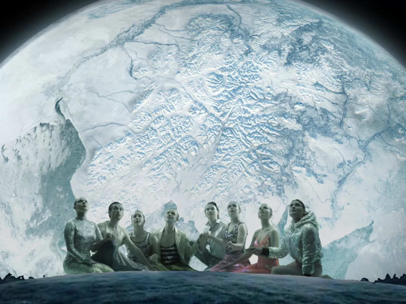 Acht Menschen in rosa und Silber gekleidet sitzen vor einem großen projizierten Mond