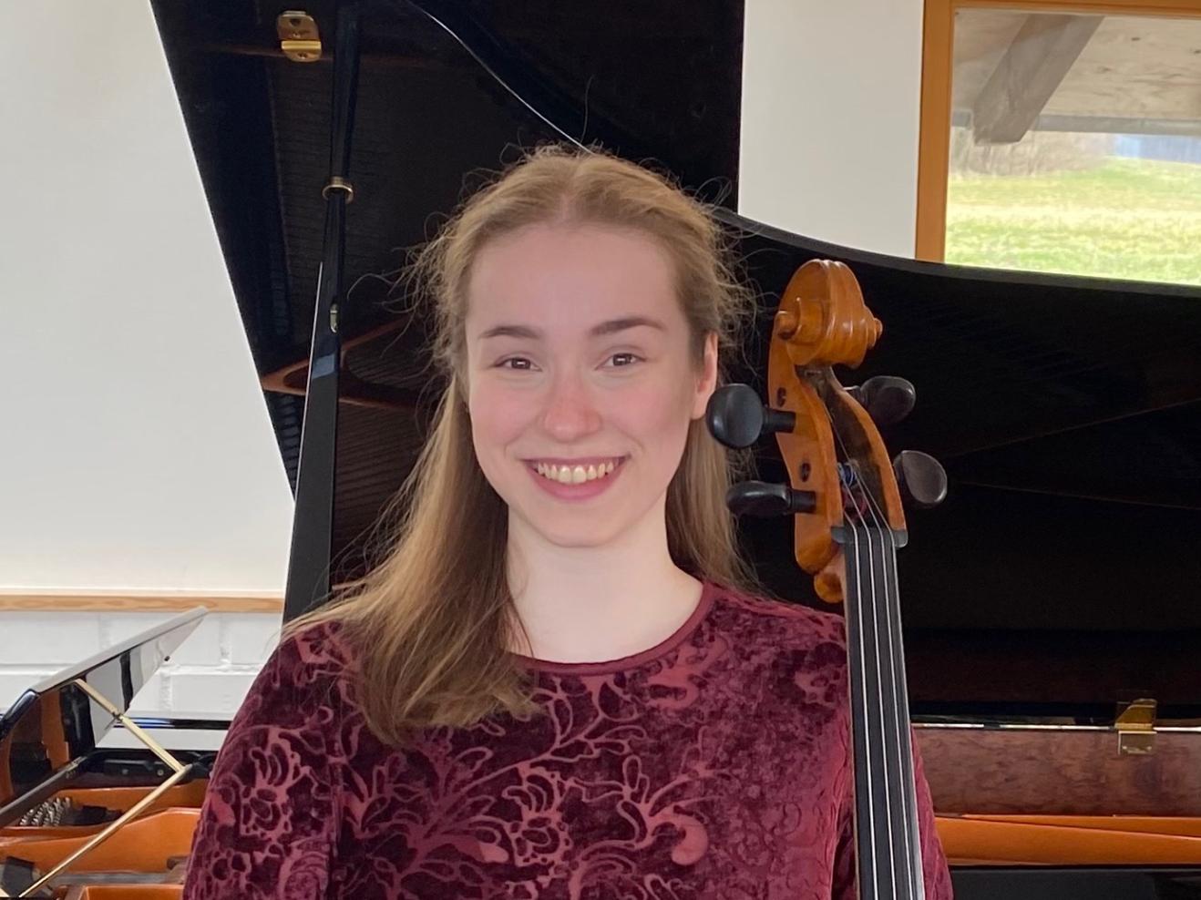 Clara Stümke lächelt in die Kamera und hält ihr Cello in der Hand.