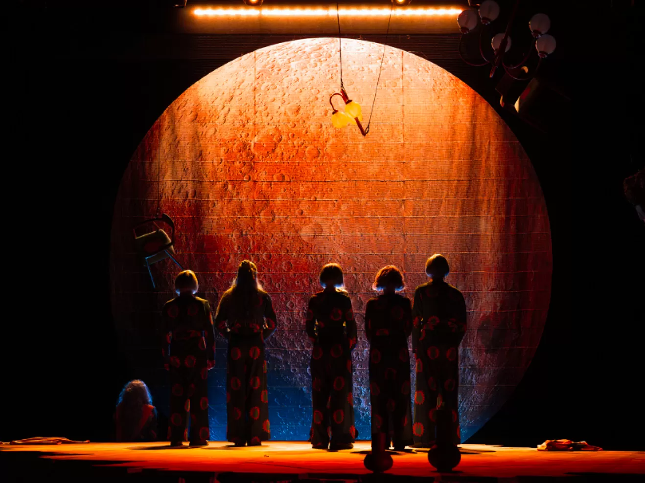 Fünf Personen stehen im Schatten. Hinter ihnen ist ein orangen angeleuchteter Mond