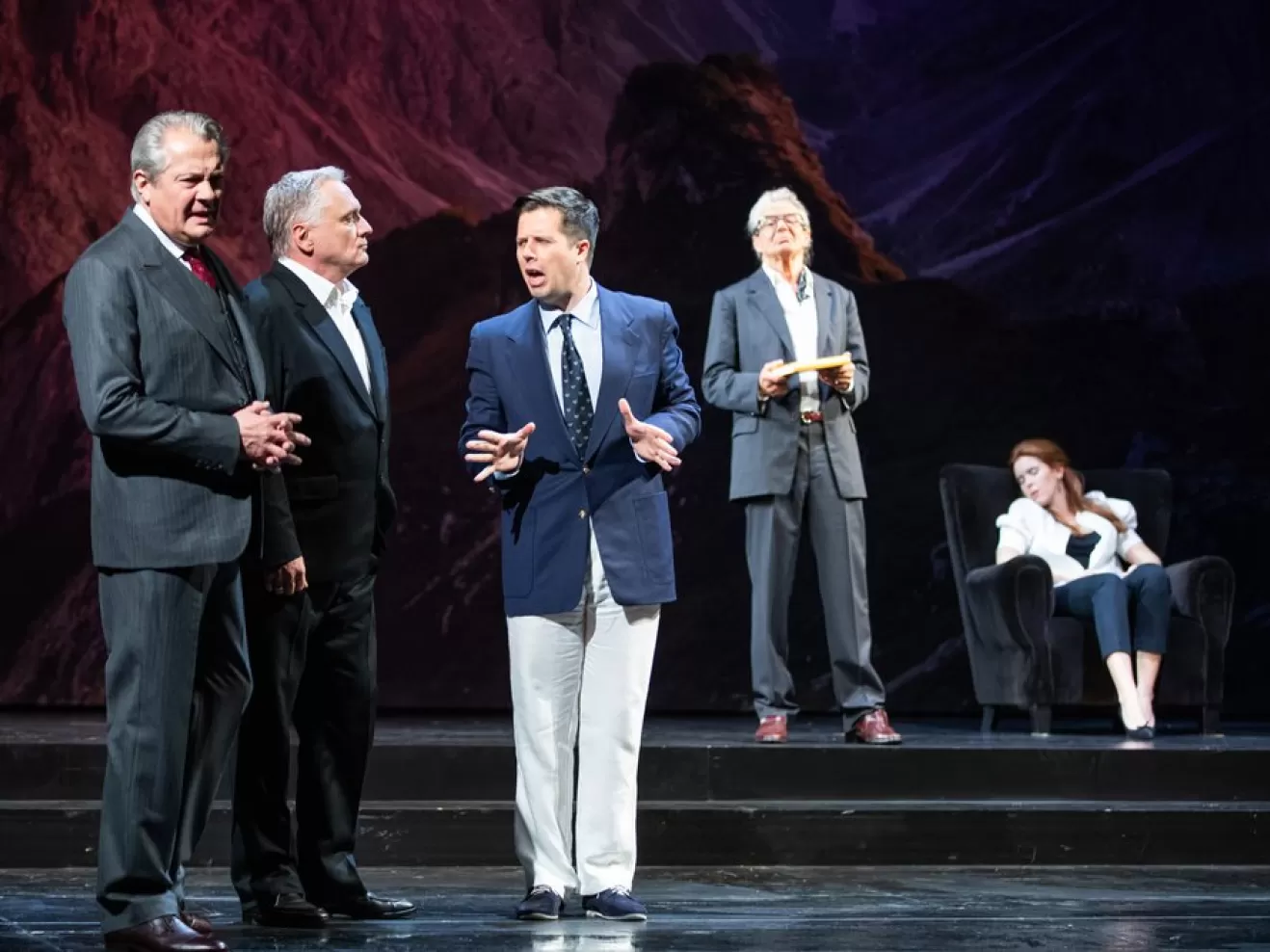 Viele Männer in Anzügen stehen auf der Bühne und reden miteinander.