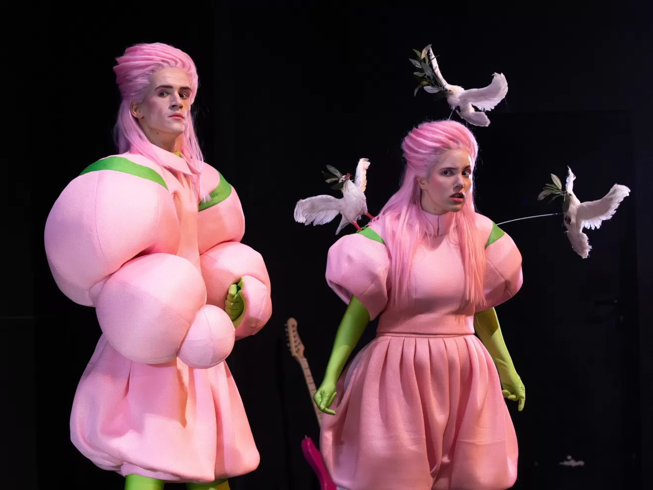 zwei Leute in pinken Aufgebauschten Anzügen schauen sich um.