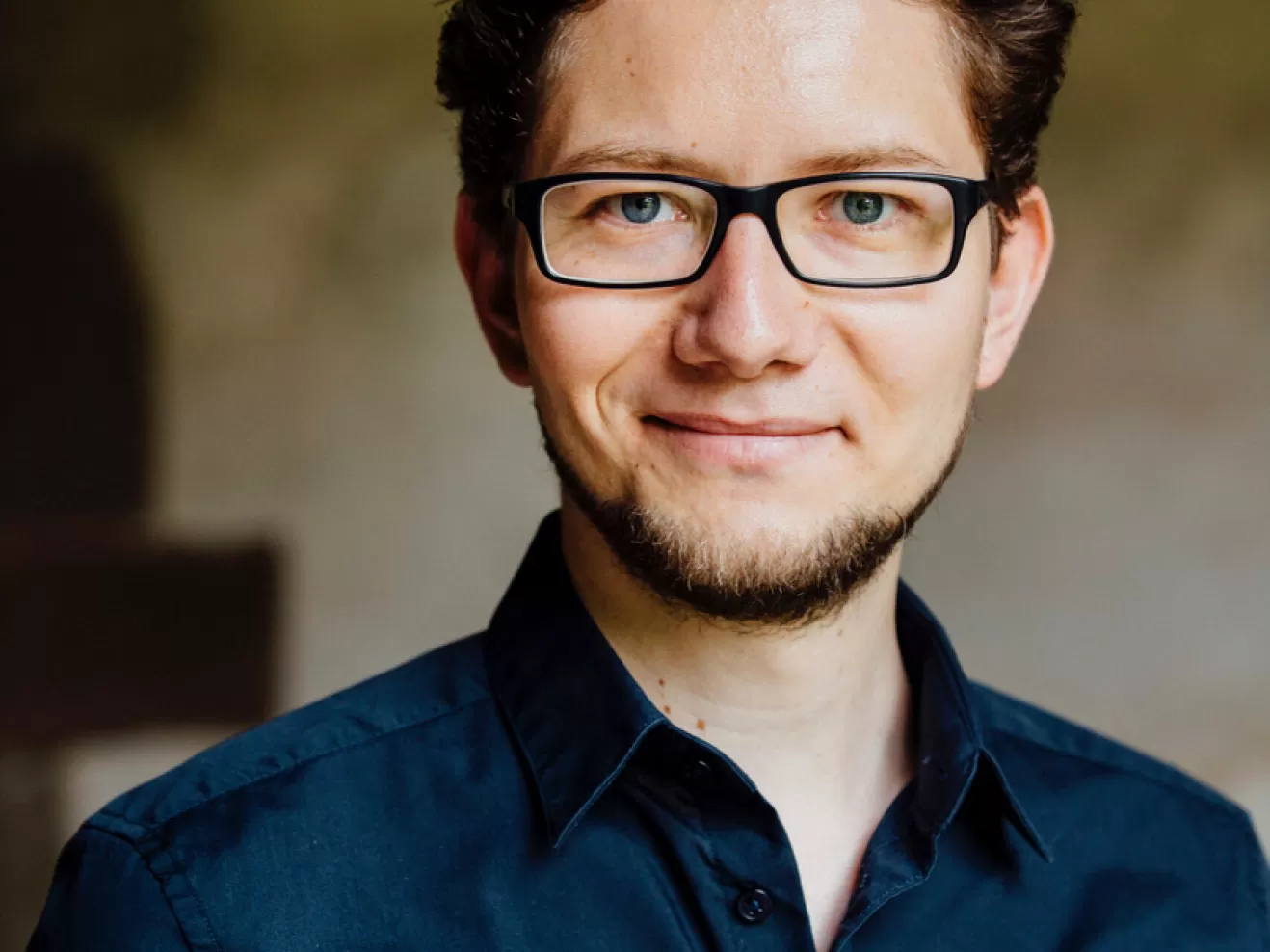 Portraitaufnahme von Benjamin Hartmann. Er trägt ein blaues Hemd und lächelt in die Kamera