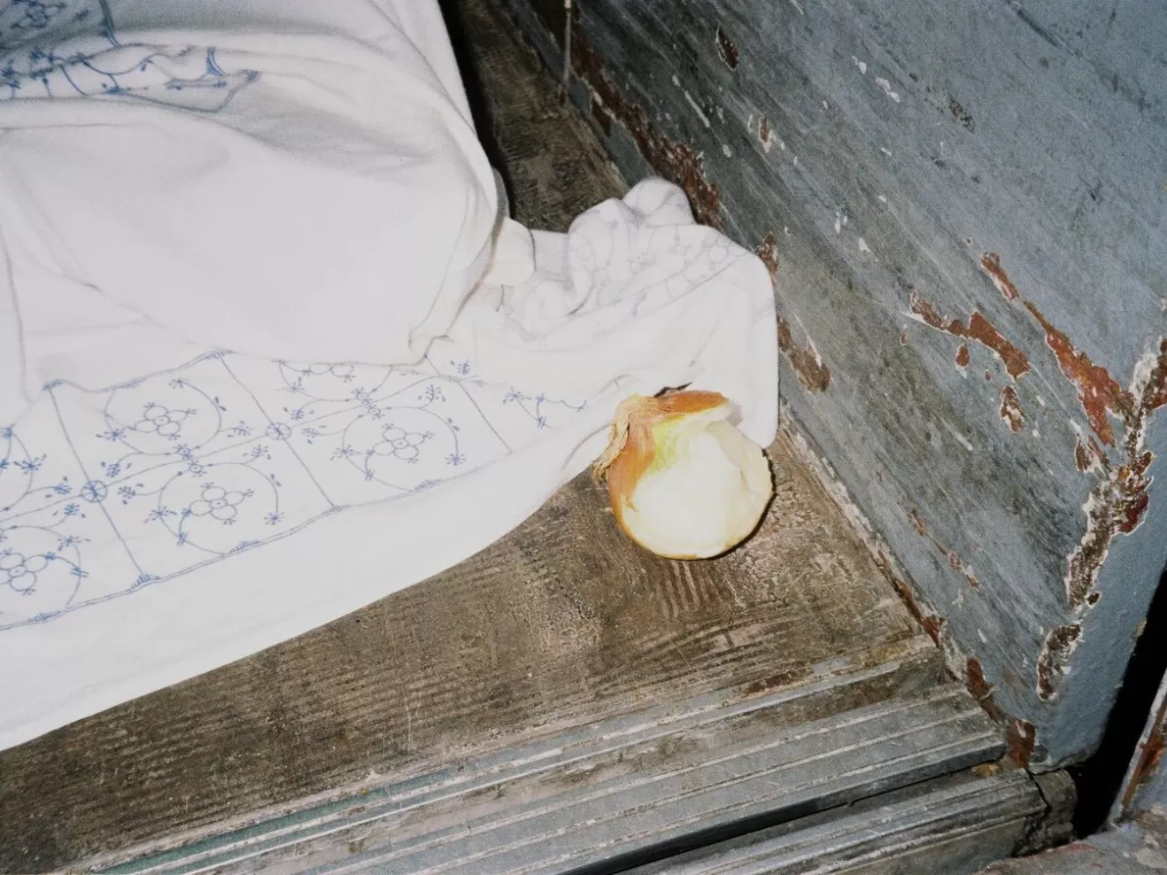 Auf einem alten Holzboden liegt eine blau-weiße Stoffdecke und daneben eine halb geschälte und angebissene Zwiebel.