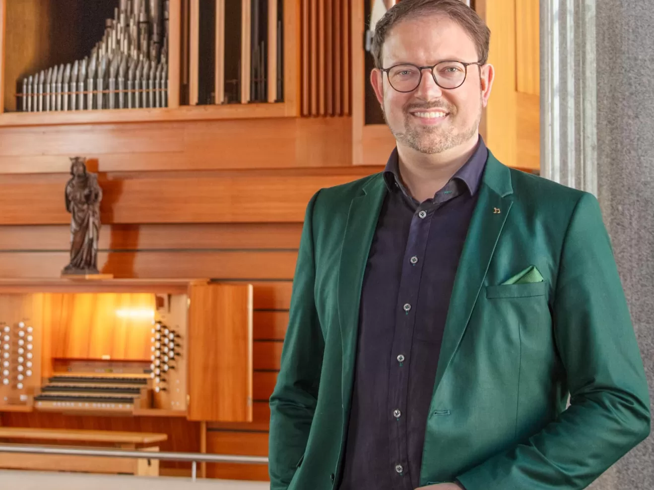 Simon Schumacher steht mit türkisem Jackett vor Orgel und lächelt in die Kamera
