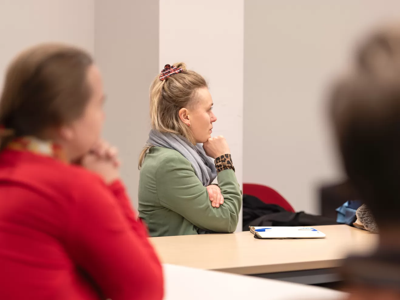 Drei Personen an einem Konferenztisch, die nach rechts blicken und einem Vortrag zuhören.