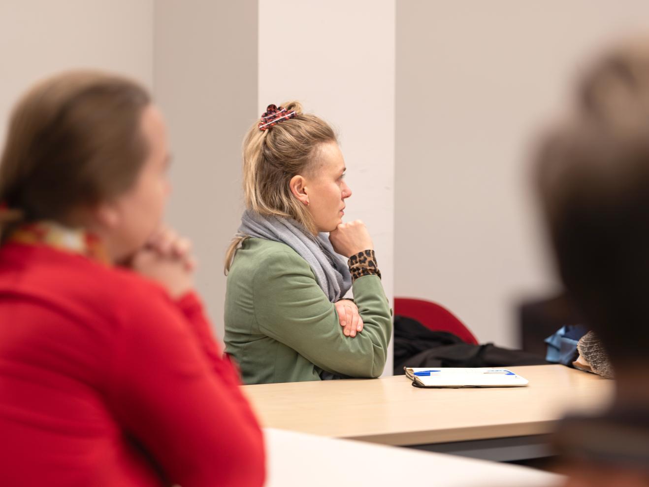 Drei Personen an einem Konferenztisch, die nach rechts blicken und einem Vortrag zuhören.