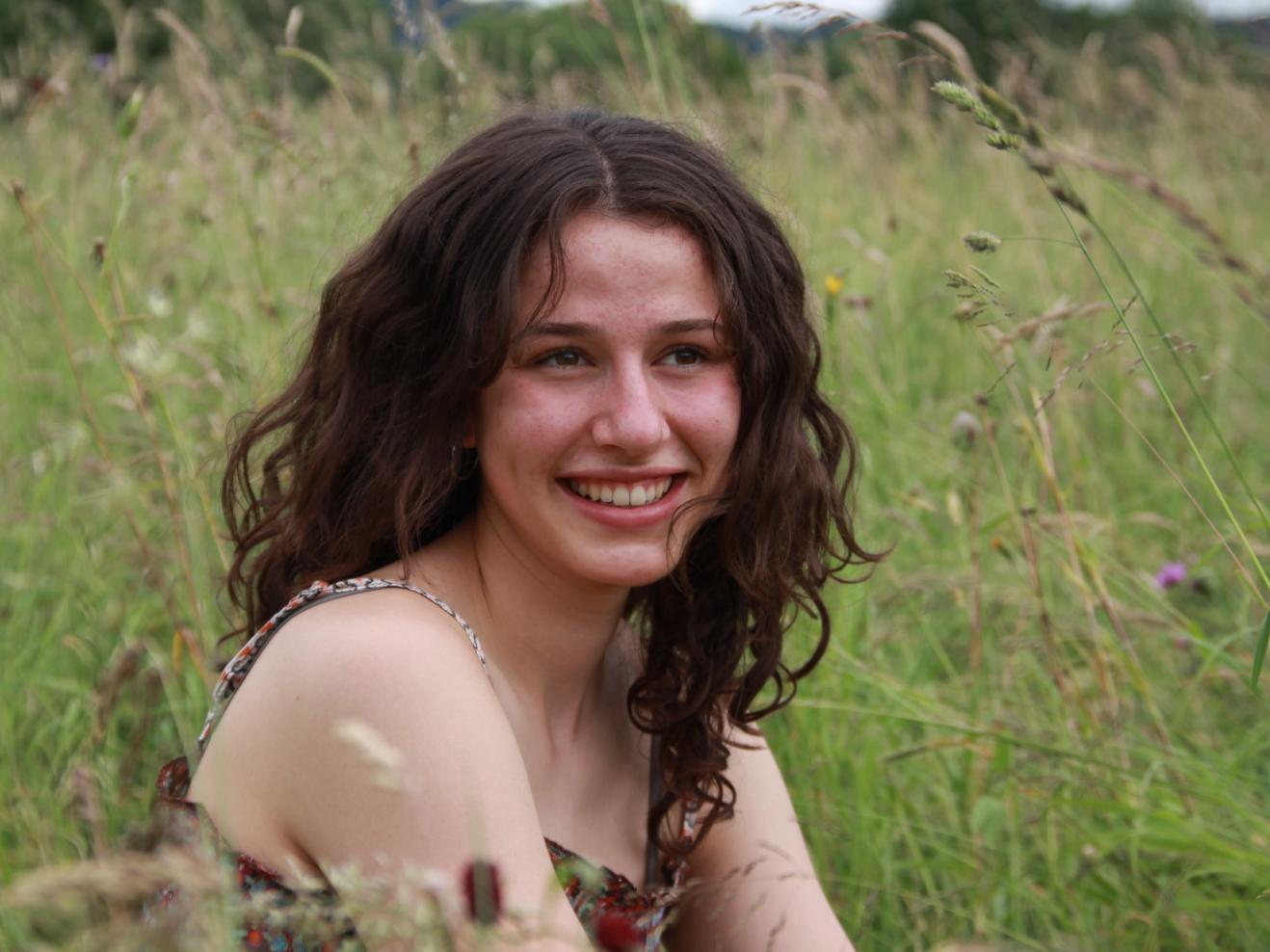 Junge Frau, die lächelnd auf einer Wiese sitzt.