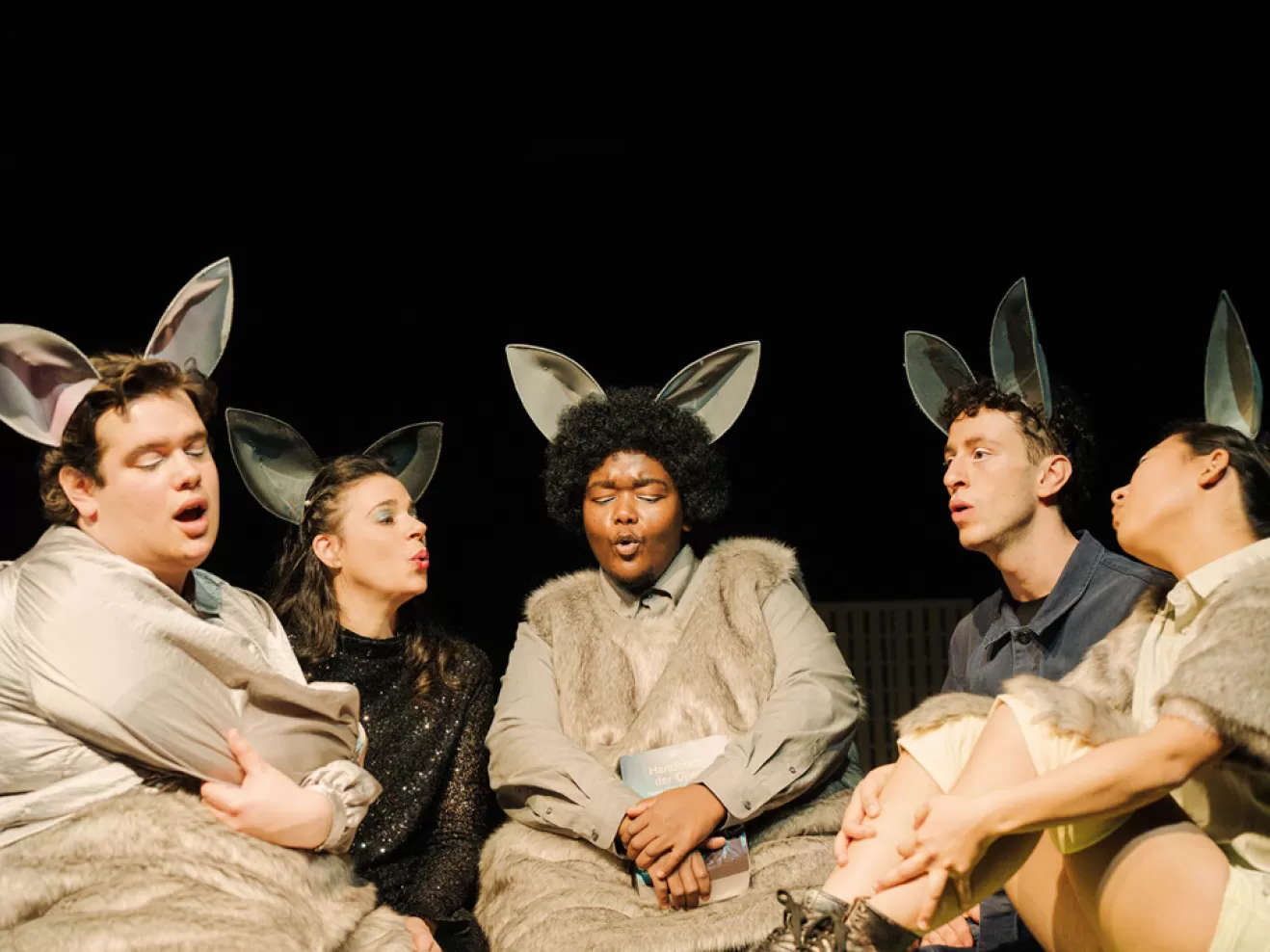 Fünf Menschen in Mäusekostümen sitzen und singen