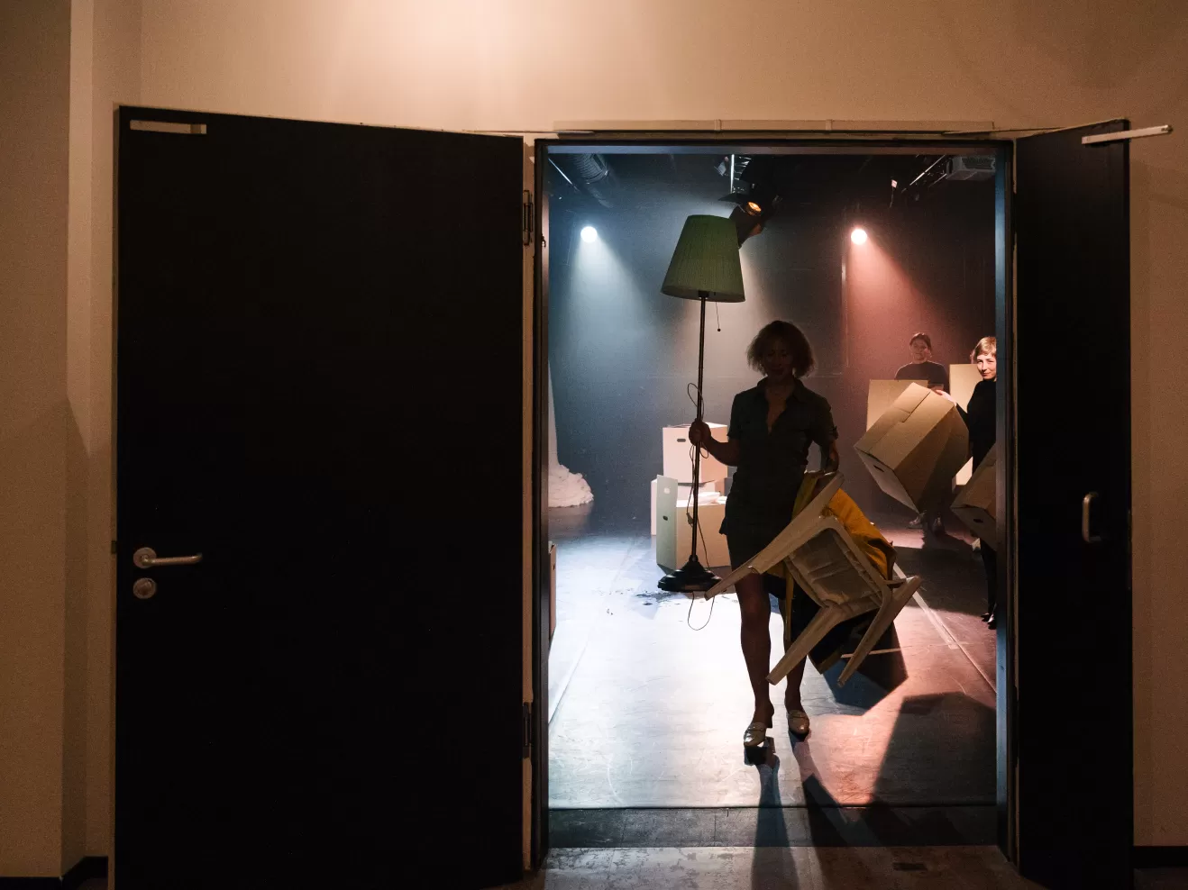 Eine Person mit Stehlampe und Umzugskarton in der Hand kommt aus einem Theatersaal.