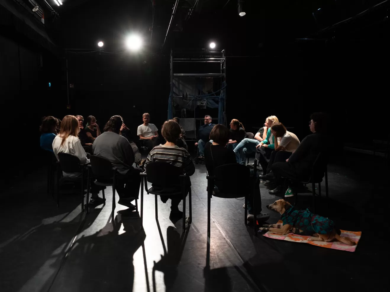 Personen sitzen in einem Stuhlkreis auf einer Bühnenfläche.