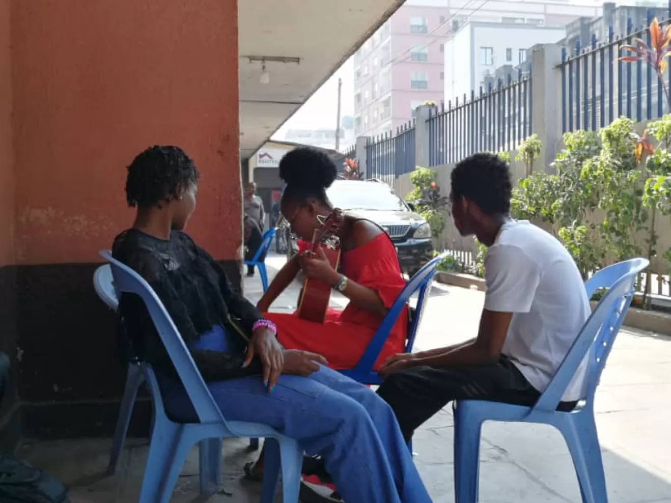 Drei Musiker*innen beim Üben in Kinshasa, sie sitzen draußen auf blauen Plastikstühlen.