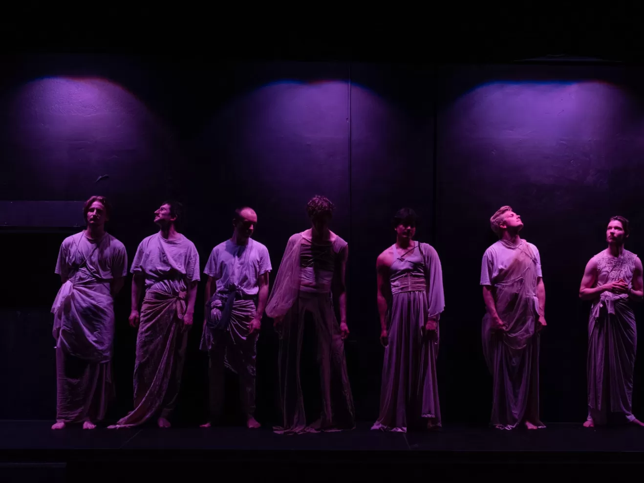 Sieben Männer in weißer Kleidung in lilafarbendem Licht.
