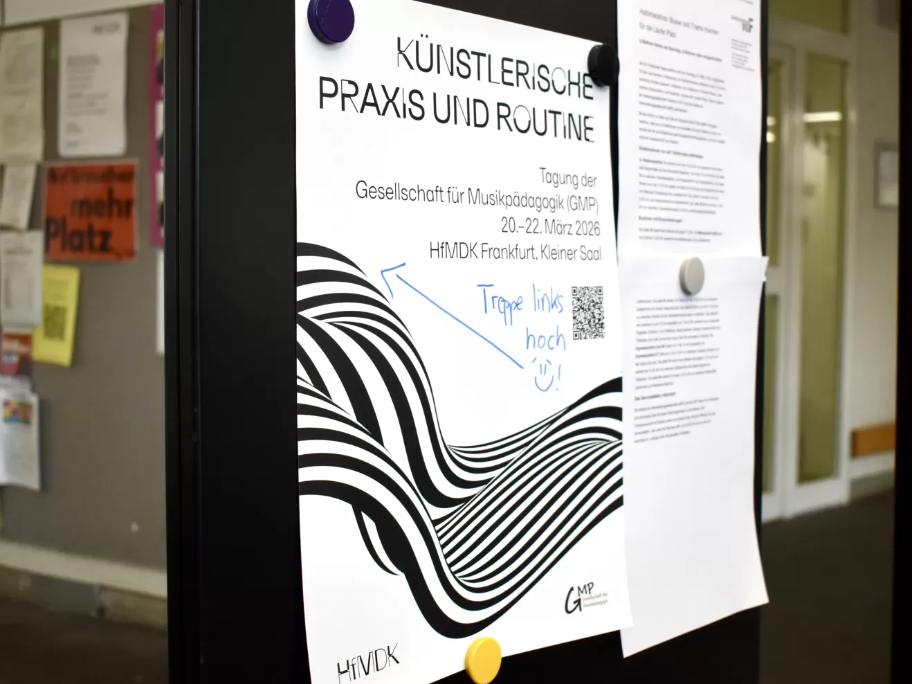 Ein Plakat an einer Magnetwand, das auf die Tagung der Gesellschaft für Musikpädagogik hinweist, mit einer handschriftlich notierten Wegweisung.