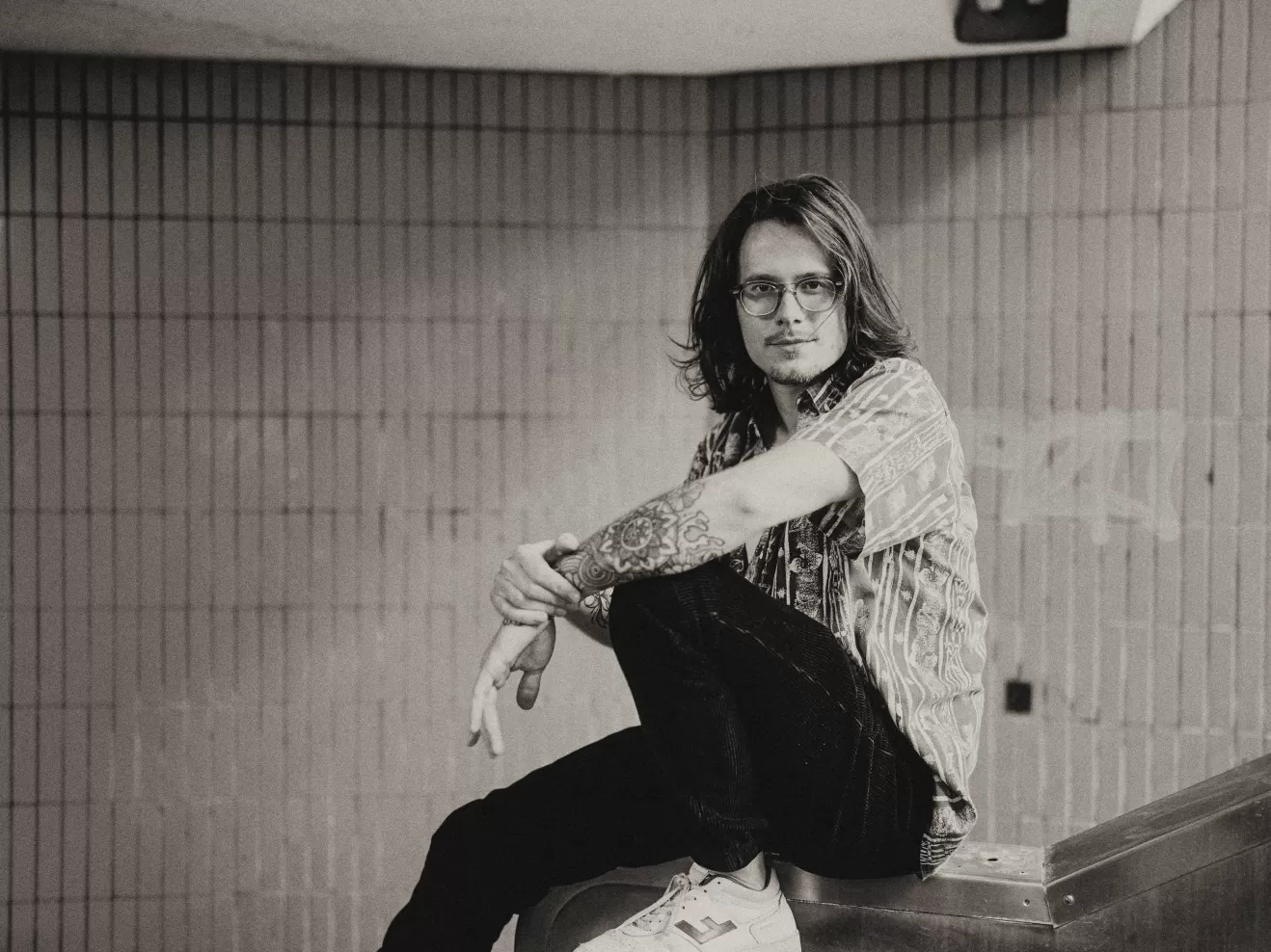 Junger Mann mit schulterlangen Haaren sitz auf einem Treppengeländer